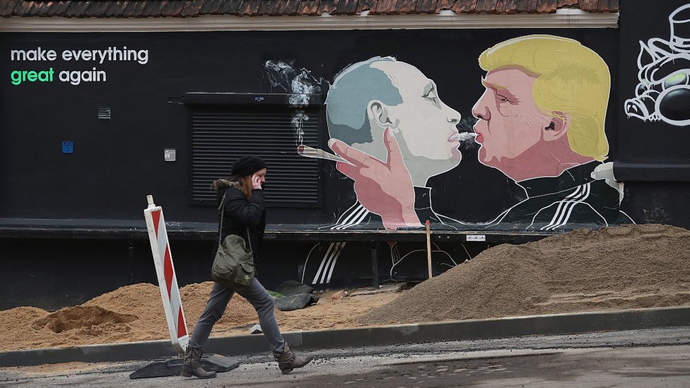 Женщина проходит мимо фрески, на которой Дональд Трамп (справа) выпускает дым марихуаны в рот Владимиру Путину в Вильнюсе, Литва