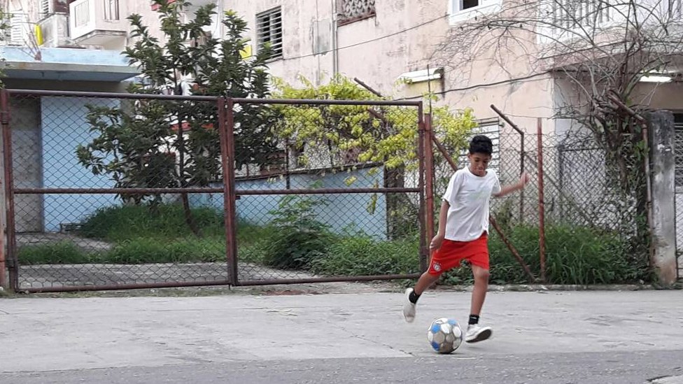 Javier juega futbol todos los días. Su portería es la entrada de un almacén de mecánica de la unidad militar que ahora está en desuso. Foto: Abraham Jiménez Enoa. Javier, de 12 años, pateando un balón.