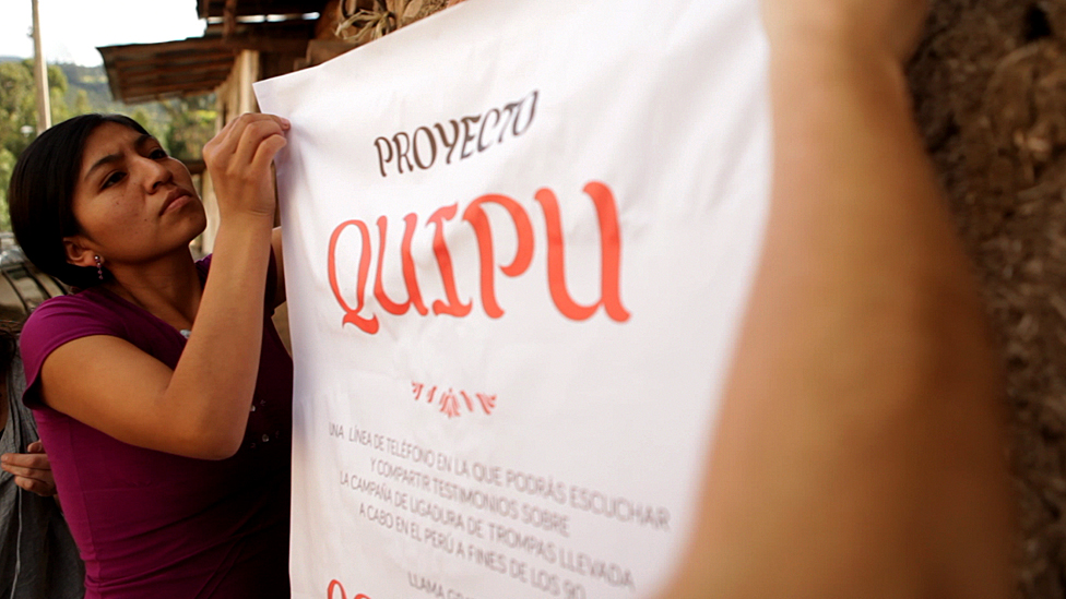 Женщина развешивает баннер, рекламирующий проект Quipu