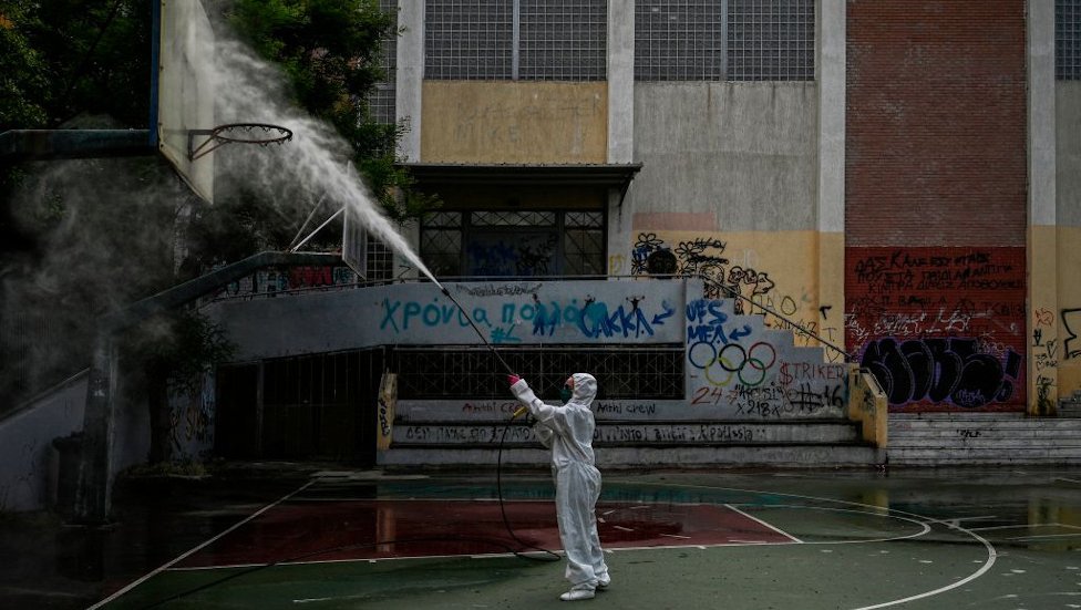 Работник муниципалитета дезинфицирует двор средней школы в Афинах