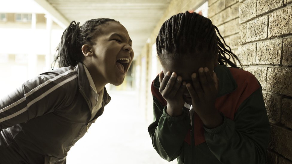 A girl shouting and another girl, who has her hand over her face