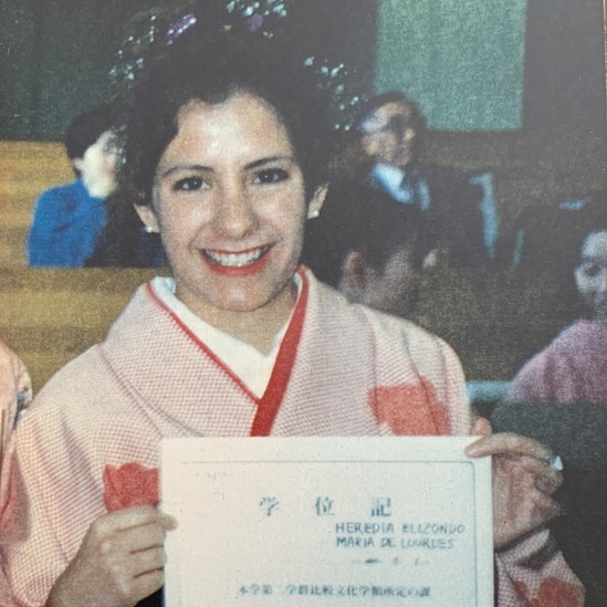 Lourdes holds up her graduation certificate