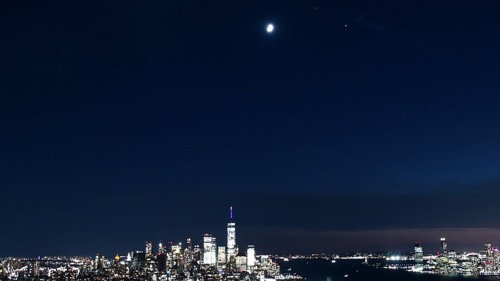 The moon, Saturn and Jupiter form a triangle as they rise over lower Manhattan and One World Trade Center