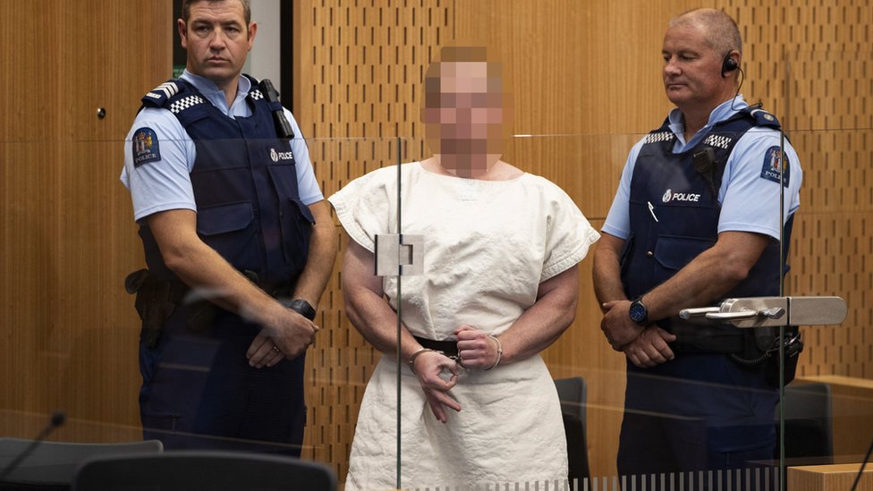 Брентон Таррант (Pixelated) делает знак в камеру во время своего появления по обвинению в убийстве в связи с резней в мечети Крайстчерча в окружном суде, Крайстчерч, Новая Зеландия, 16 марта 2019 г., переиздано 5 апреля 2019 г.