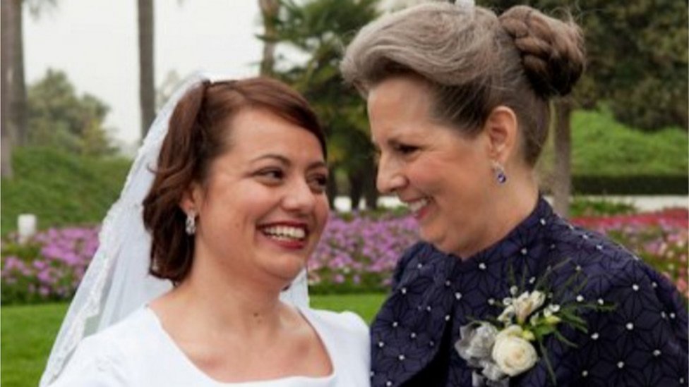 Sarah on her wedding day in a veil smiling next to her mother