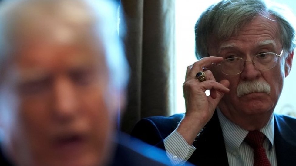 John Bolton se ajusta los anteojos mientras mira al presidente Trump
