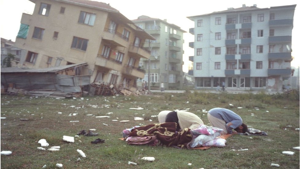 Unos hombres rezan frente a unos edificios destruidos por el terremoto de Izmit de 1999.