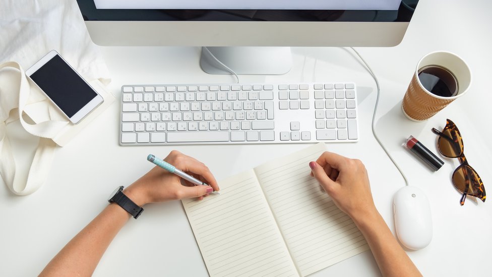 Una persona escribiendo con la mano izquierda frente a una computadora.