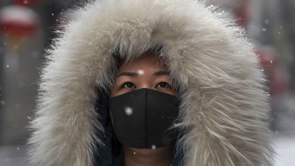 A woman wears a protective mask during a snowfall in Beijing