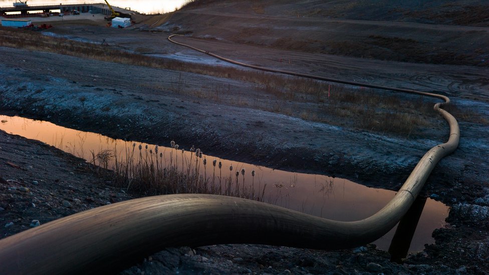 Водозаборная труба для операций с нефтеносными песками ведет вниз к реке Атабаска 28 апреля 2015 года к северу от Форт МакМюррей, Канада. Fort McMurray в настоящее время справляется с экономическим спадом из-за низких цен на нефть, и большая часть увольнений сказывается на временной рабочей силе. Ожидается, что в 2015 году нефтегазовая промышленность Канады потеряет 37% доходов.