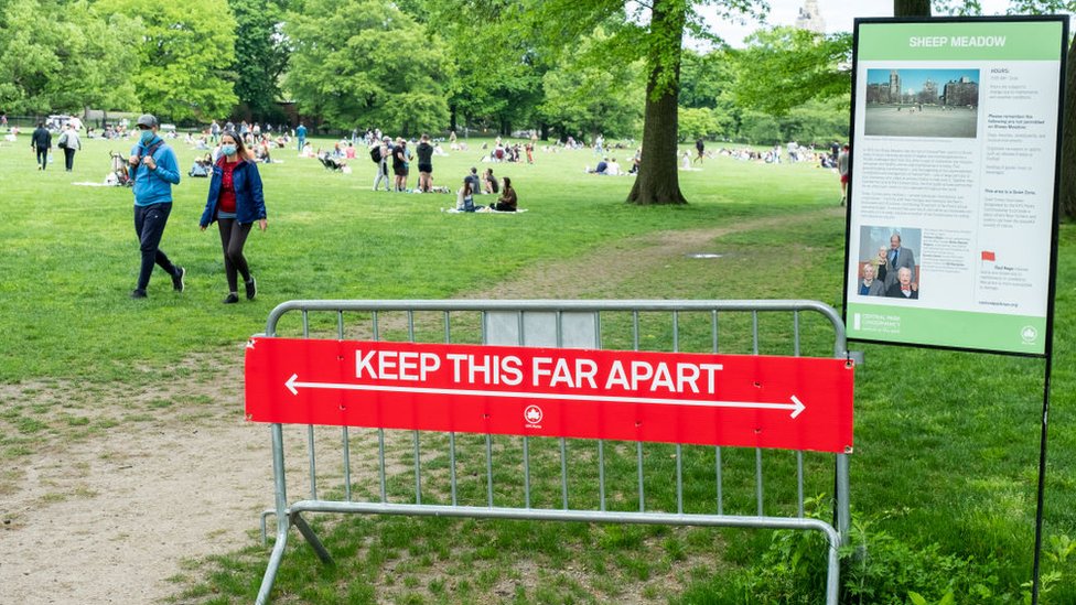 В выходные, посвященные Дню поминовения, вывеска у входа в Sheep Meadow в Центральном парке гласит: «Держитесь подальше», физически показывая, как далеко находится 6 футов от толпы людей в стороне от парка