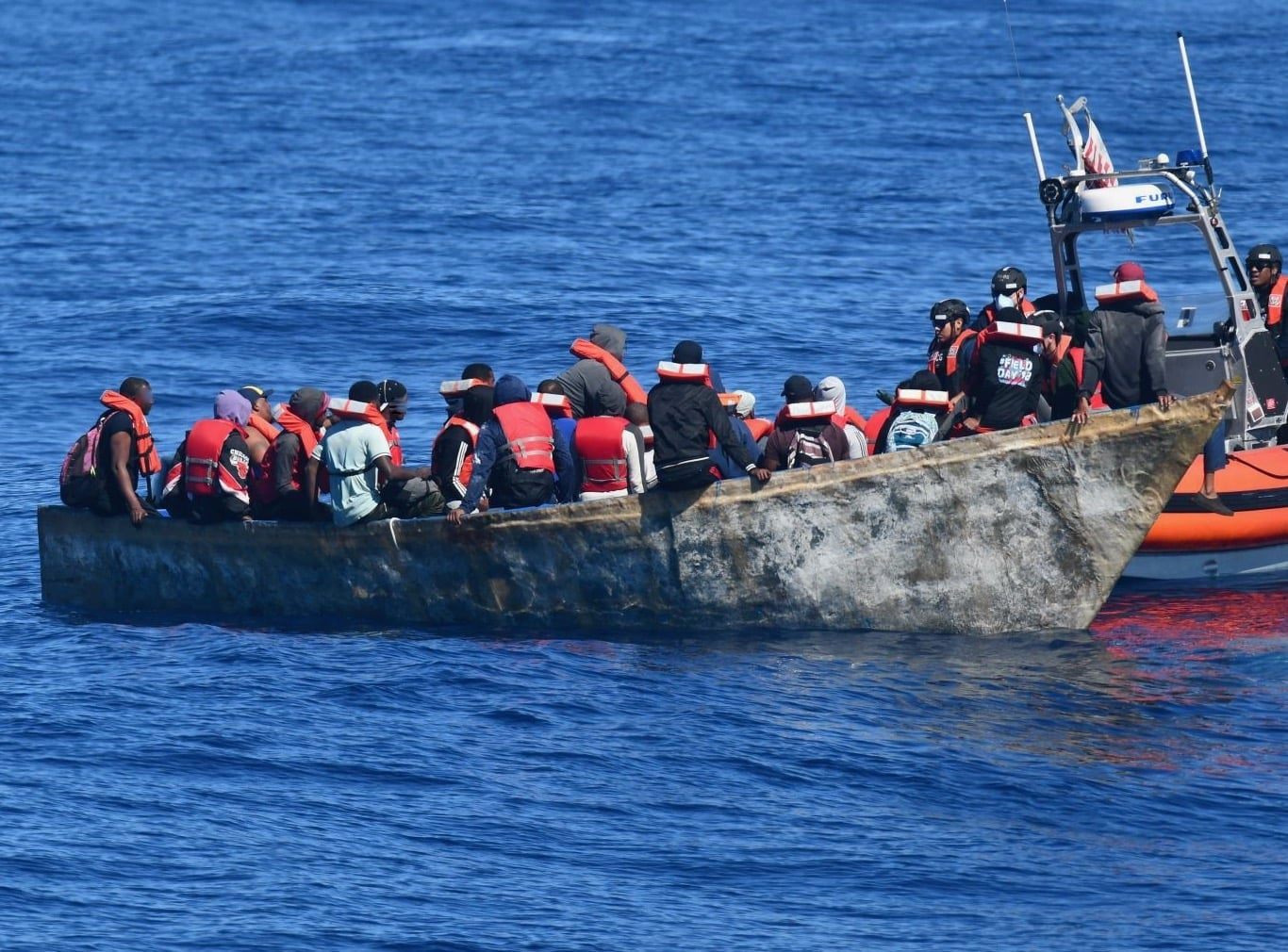 Migrantes detenidos por la Guardia Costera de EE.UU. en el Canal de la Mona. Están en un bote de madera junto a otra embarcación que pertenece al cuerpo militar.