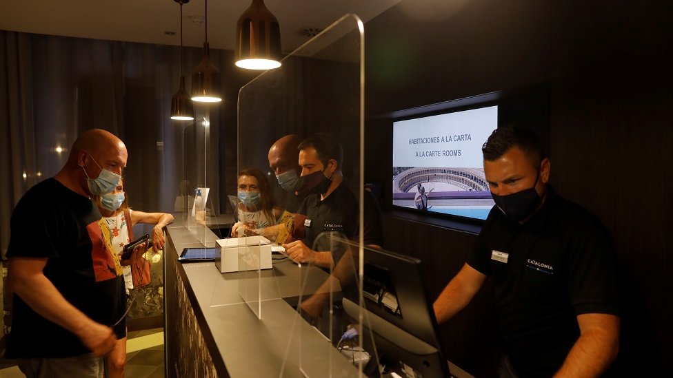 German tourists are attended by receptionists, wearing protective face mask as they do the check-in at the Catalonia Ronda hotel, in southern Spain