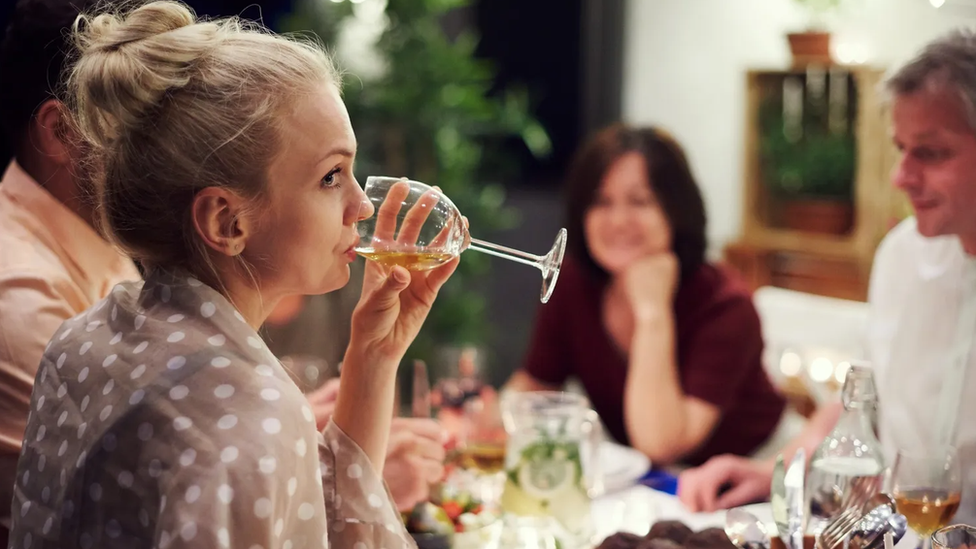 Mujer bebiendo vino en una cena.