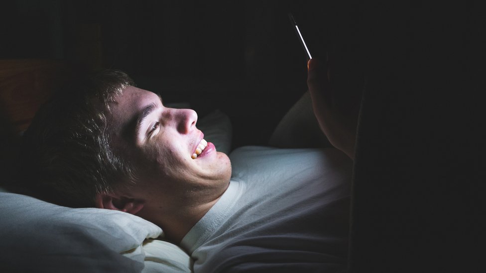 Подросток смотрит в свой телефон в темноте в постели