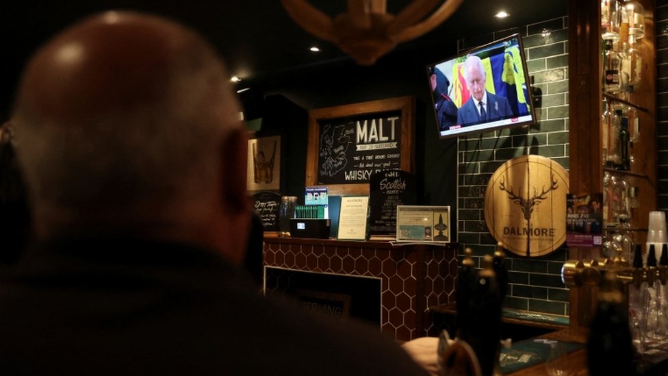 Homem de costas observa TV no canto de um pub