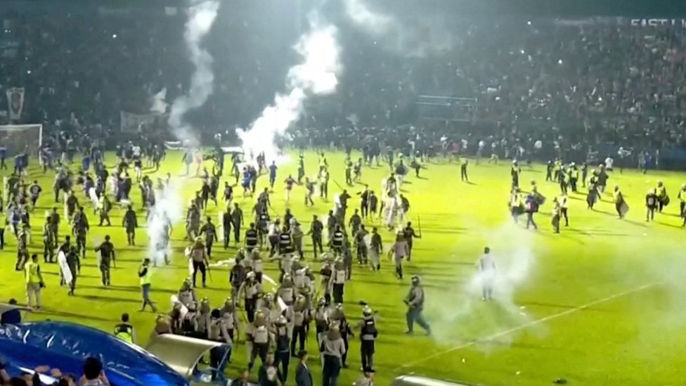 A screenshot of video vision shows hundreds of fans running on the field amid clouds of tear gas
