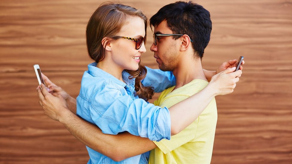 Una pareja se abraza y al mismo tiempo chatea.