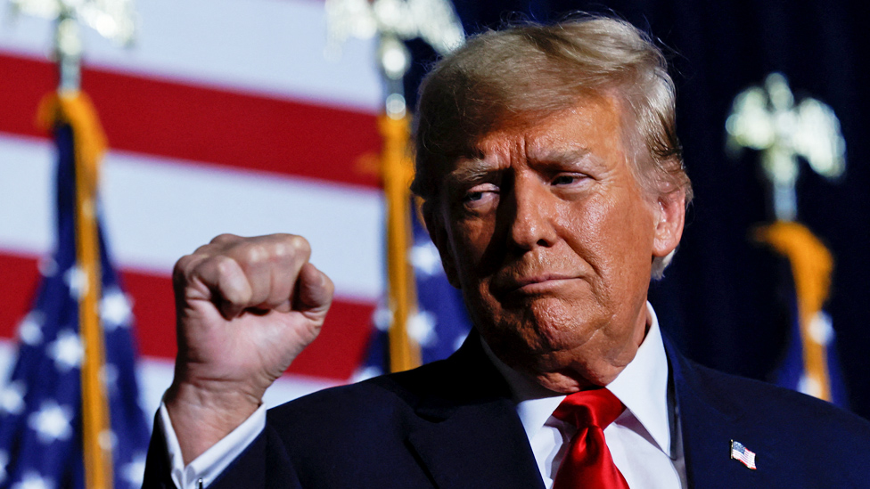 Donald Trump pumps his fist while standing in front of US flags