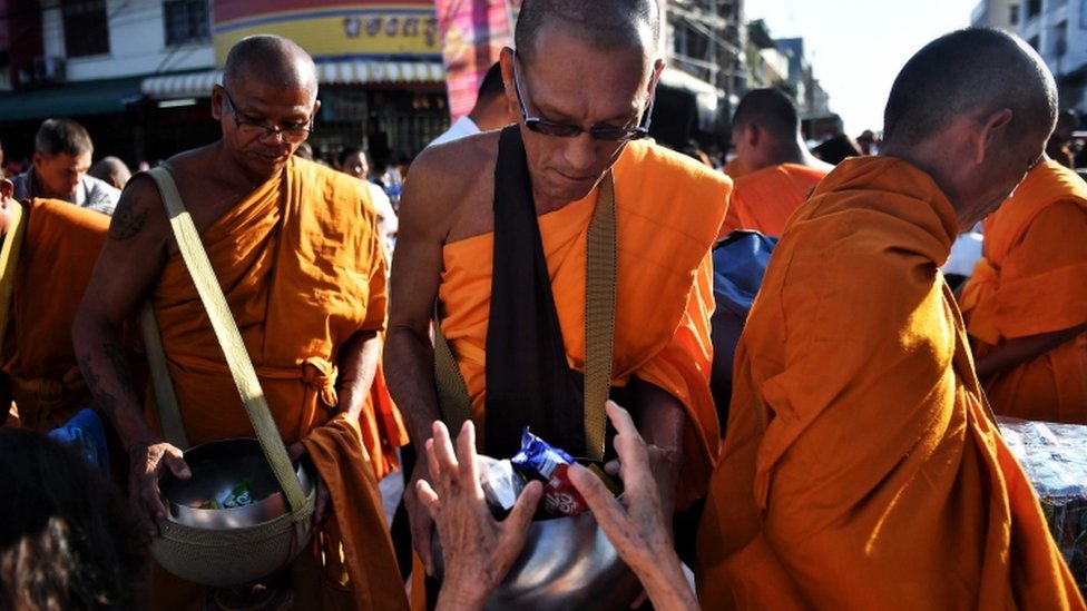 Люди подают милостыню буддийским монахам во время массовой молитвы через неделю после того, как одинокий солдат застрелил 29 человек в Таиланде
