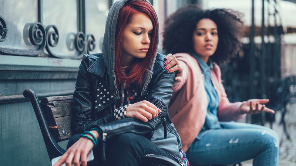 A woman puts her hand on the shoulder of another woman who seems angry or offended