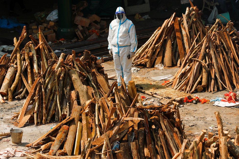 A man wearing personal protective equipment (PPE) stands next to funeral pyres in New Delhi, India