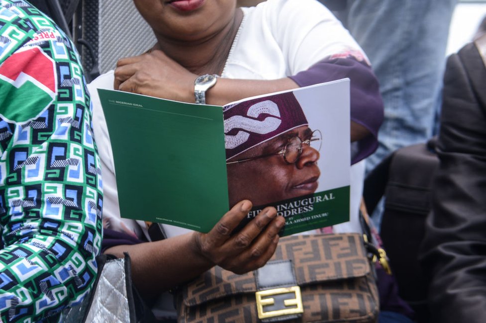 امرأة تنظر إلى كتيب رسمي يظهر وجه بولا تينوبو في حفل تنصيبه في أبوجا، نيجيريا - الاثنين 29 مايو/ أيار 2023