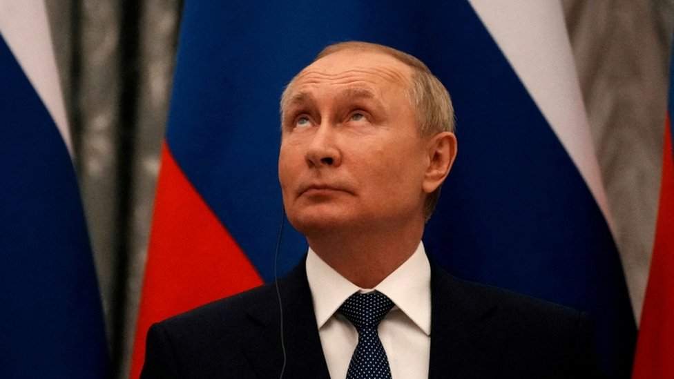 Putin olhando para cima, em frente a bandeira, durante evento