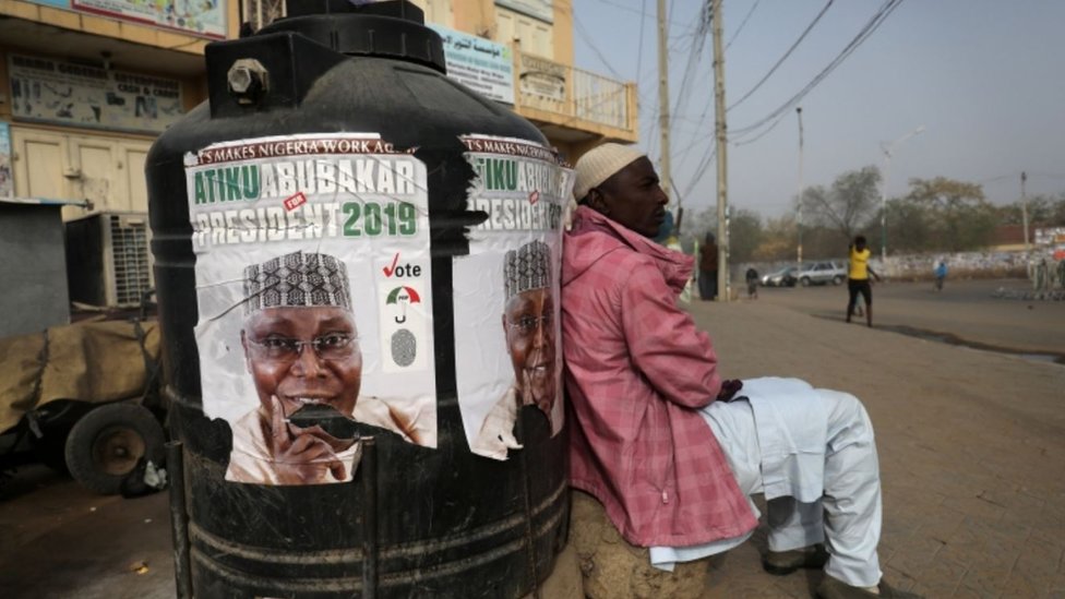 Мужчина сидит рядом с плакатом кампании Атику Абубакара, лидера Народно-демократической партии (НДП), после переноса президентских выборов в Кано, Нигерия, 17 февраля 2019 г. REUTERS / Luc Gnago