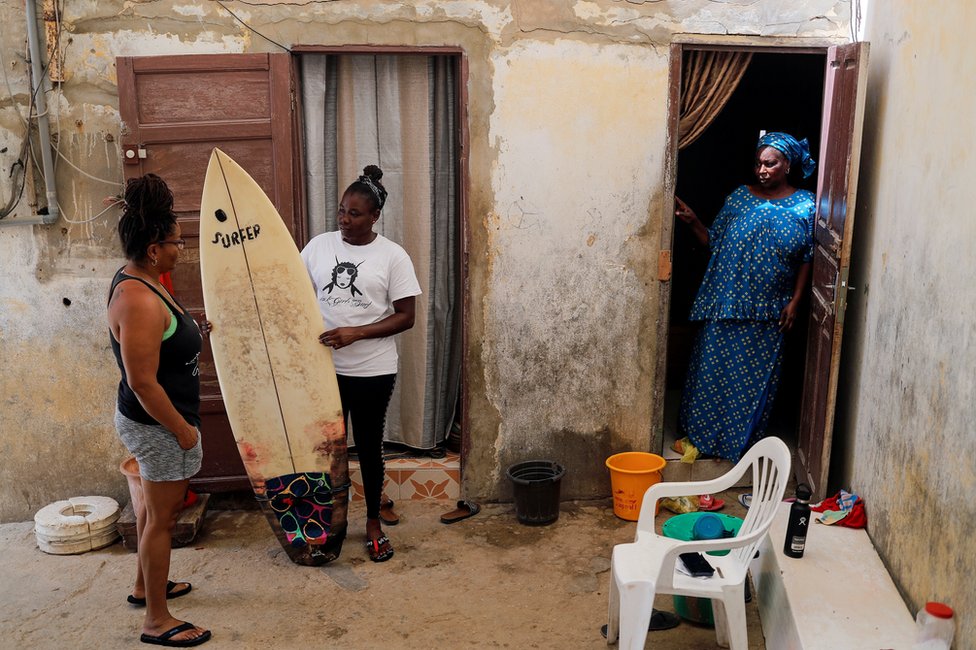 Khadjou Sambe stands with her surboard as she talks to her coach Rhonda Harper as her mother looks on