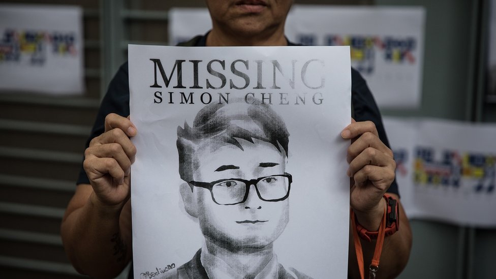 A woman holds a poster showing a portrait of British consulate worker Simon Cheng, who was detained