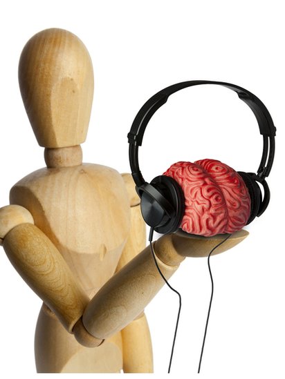 La música está ayudando a algunos científicos a entender el cerebro no solo de personas con demencia, sino también cerebros sanos. Muñeco de madera sosteniendo en una mano un cerebro con audífonos.