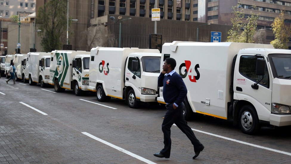 Работник, занимающийся перевозкой наличных, проходит мимо бронированных автомобилей, припаркованных на улице во время общенациональной акции протеста после серии смертельных ограблений в этом году в Йоханнесбурге, Южная Африка, 12 июня 2018 г.