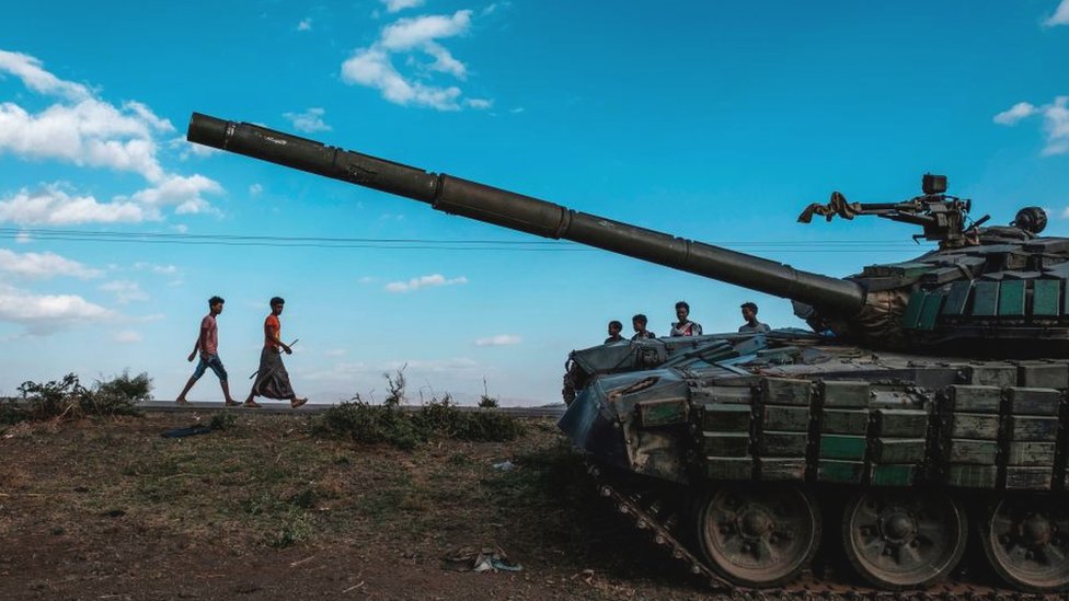 Молодые люди идут рядом с заброшенным танком, принадлежащим силам Тиграяна к югу от города Мехони, Эфиопия - 11 декабря 2020 года
