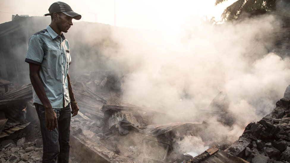 Мужчина стоит перед сгоревшим домом в районе PK5 в Банги 26 декабря 2019 года после того, как вспыхнули столкновения, когда торговцы взяли в руки оружие, чтобы противостоять налогам, взимаемым группами ополченцев.