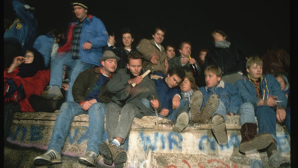 Una docena de personas celebran la apertura de la frontera encima del Muro de Berlín.
