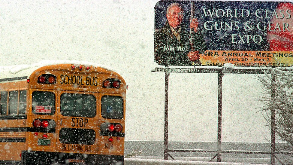 A school bus passes an NRA advertisement.