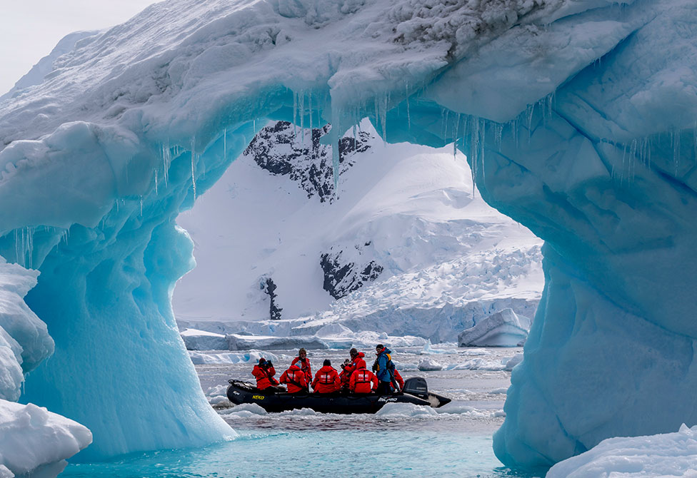 Tourists exploring an iceberg arch in Cierva Cove along the west coast of Graham Land, Antarctic Peninsula, Antarctica