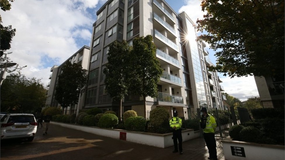 Police officers stand outside a block of flats where a boy and two adults died