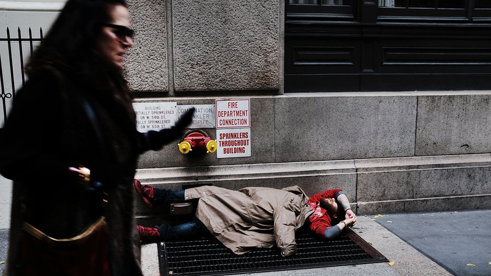 Una mujer pasa caminando cerca de un hombre sin techo en Nueva York.