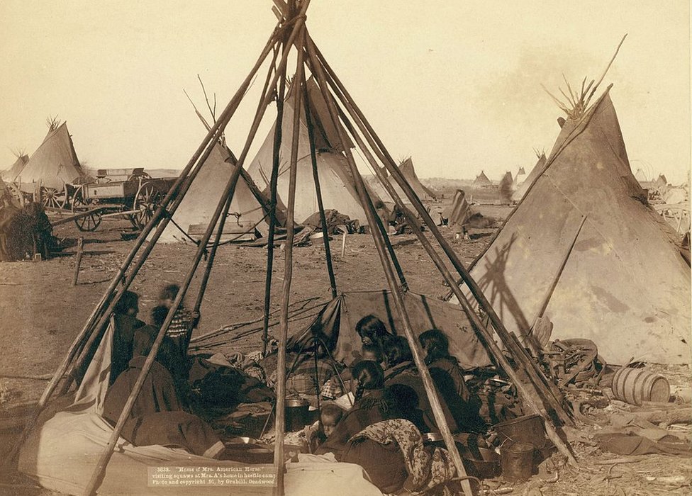 Mujeres y niños oglala sentados dentro de la estructura sin cubrir de un tipi, en o cerca de la Reserva de Pine Ridge, en 1891. Foto de John C. H.Grabill.