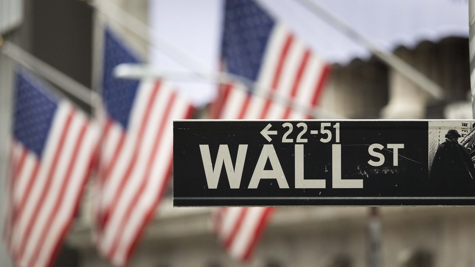 Cartel de la calle Wall Street en Nueva York con un fondo de banderas de Estados Unidos