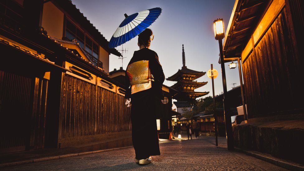 Mujer japonesa recorriendo calles poco iluminadas.