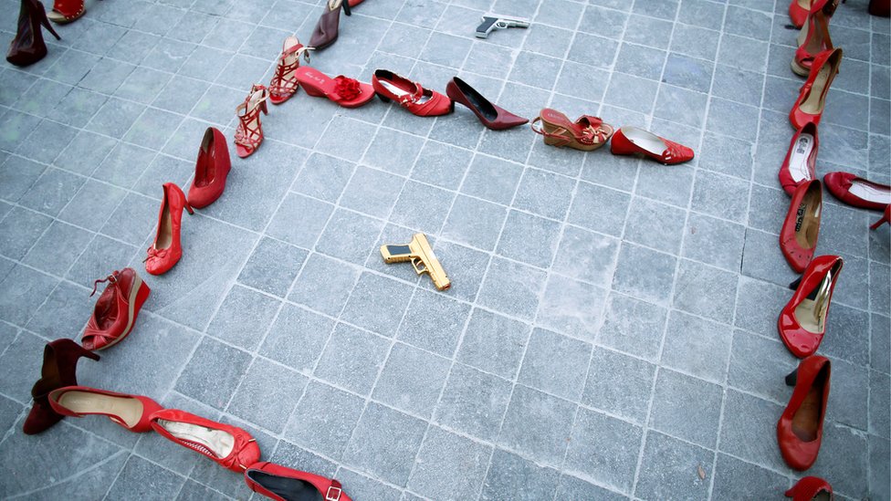 Пары женских красных туфель выставлены рядом с игрушечным пистолетом во время акции протеста «День без женщин»