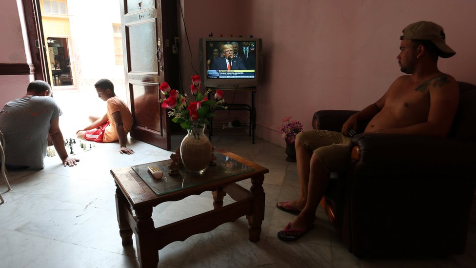 Varias cadenas internacionales transmitieron el discurso de Trump en Cuba. Un cubano ve el discurso de Trump desde el televisor de su casa mientras dos jóvenes juegan ajedrez en el portal de la casa.