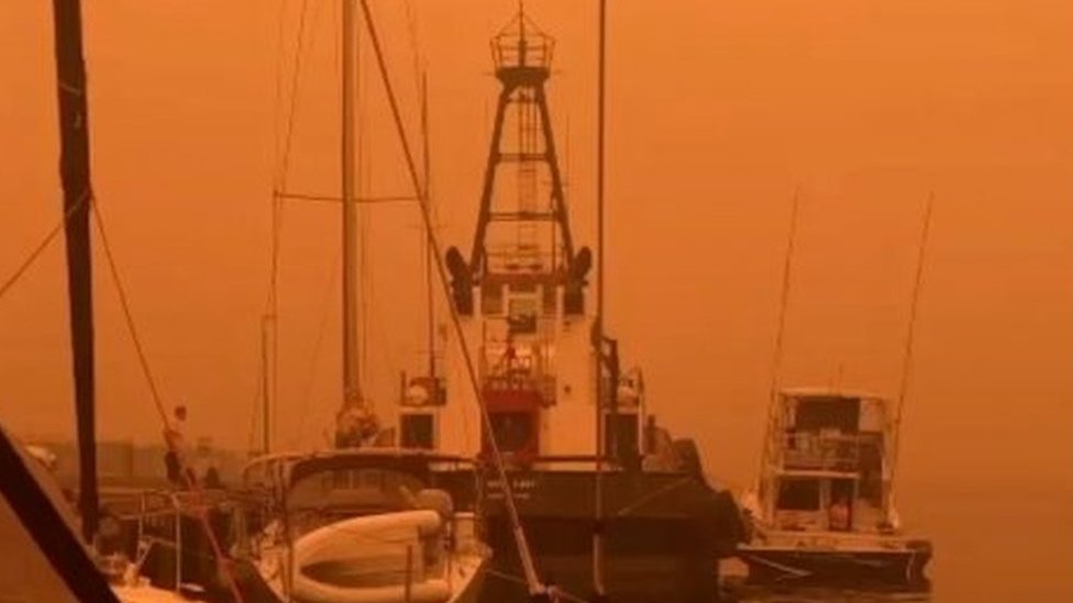 An orange sky shrouds boats at a wharf in Eden, NSW