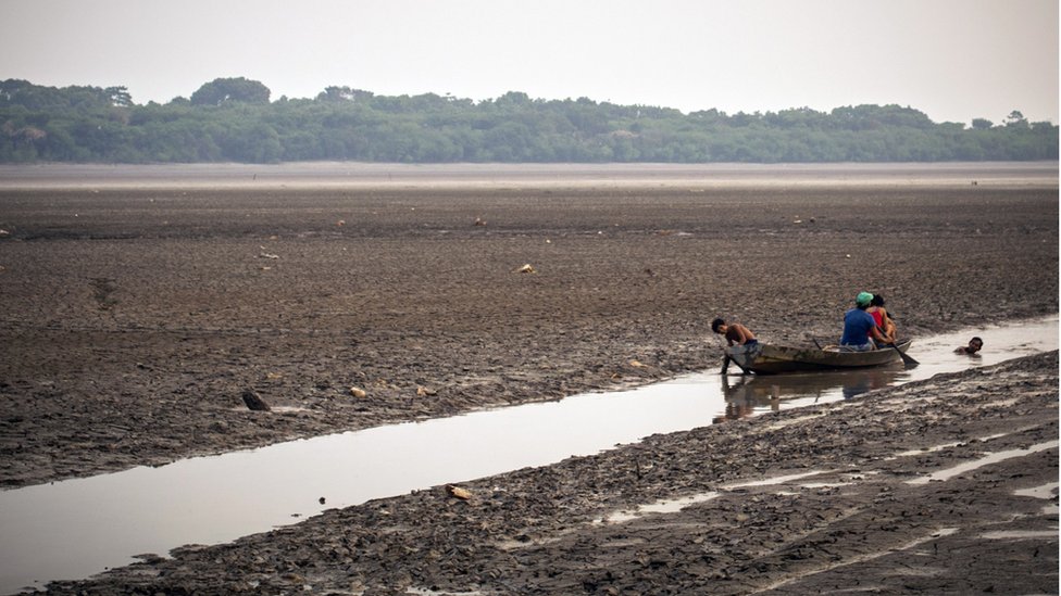 Pessoas em canoa em trecho bastante raso e estreito de rio