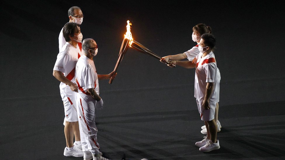 The torch carriers exchange the flame of the Olympic torch during the Opening Ceremony of the Tokyo 2020 Olympic Games at Olympic Stadium on July 23, 2021 in Tokyo, Japan.