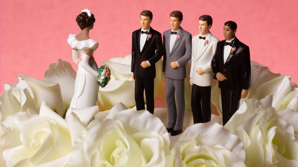 A wedding cake with figures of a bride and three grooms