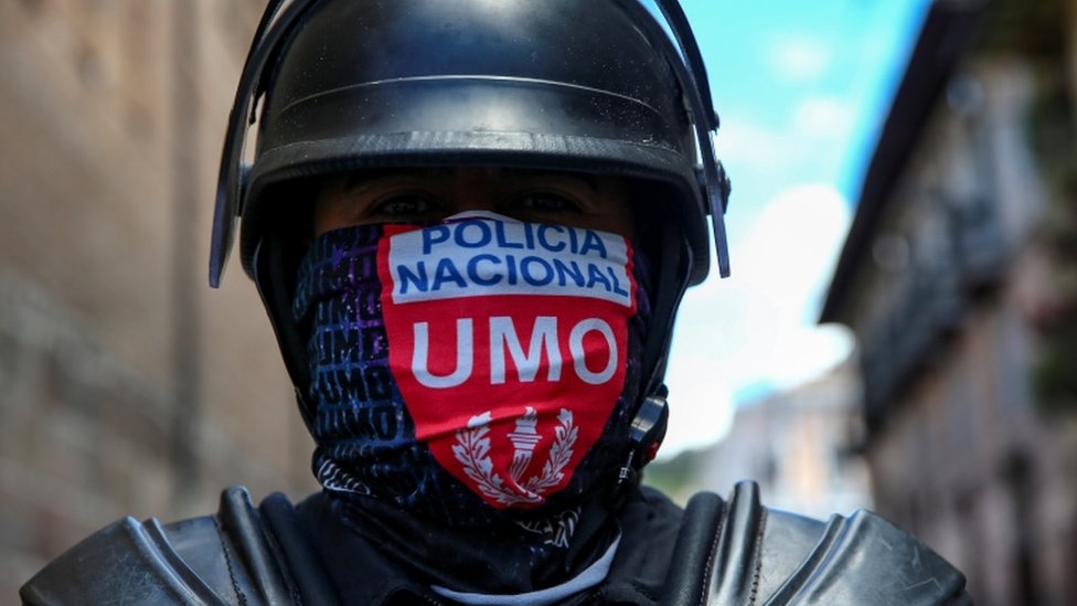 Сотрудник национальной полиции носит маскировку во время протестов в Кито